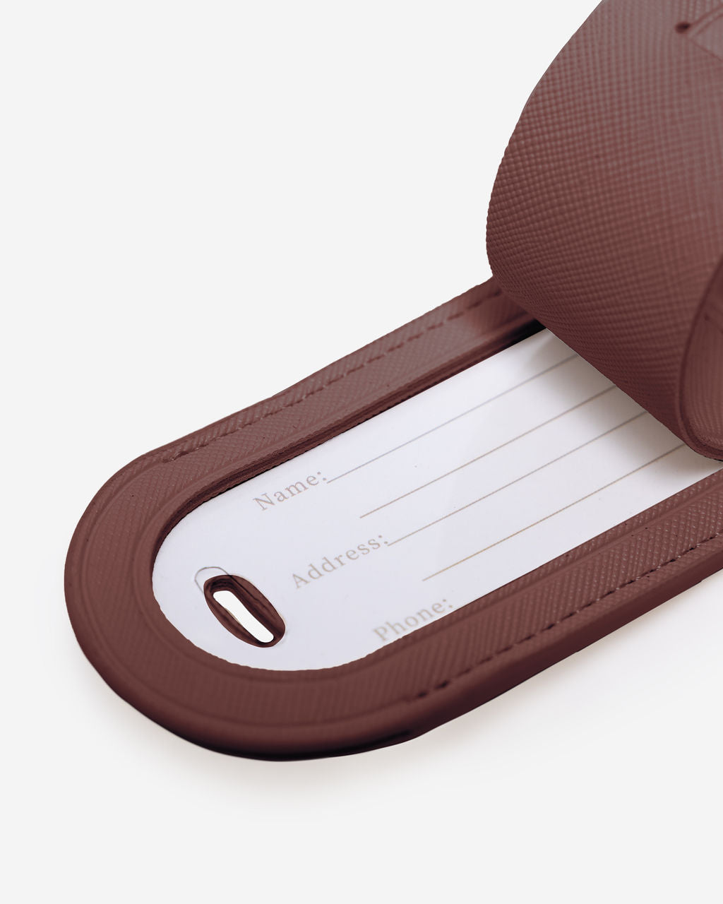 Close-up of a brown leather luggage tag displaying the internal white card with fields for Name, Address, and Phone number.
