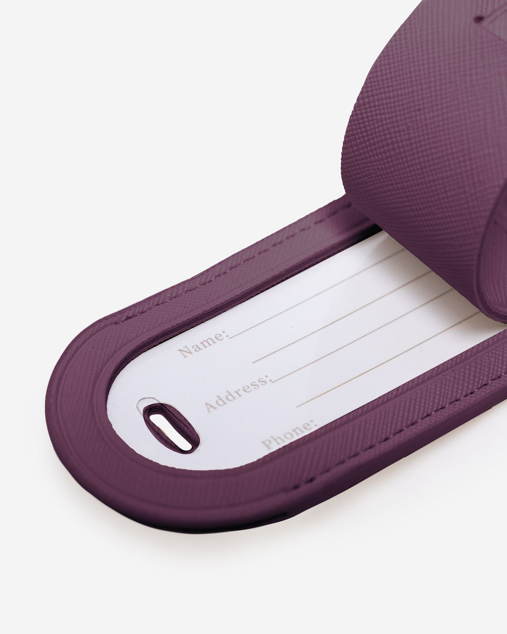 Close-up of a burgundy-colored Saffiano leather luggage tag with the internal white card showing fields for "Name:", "Address:", and "Phone:".