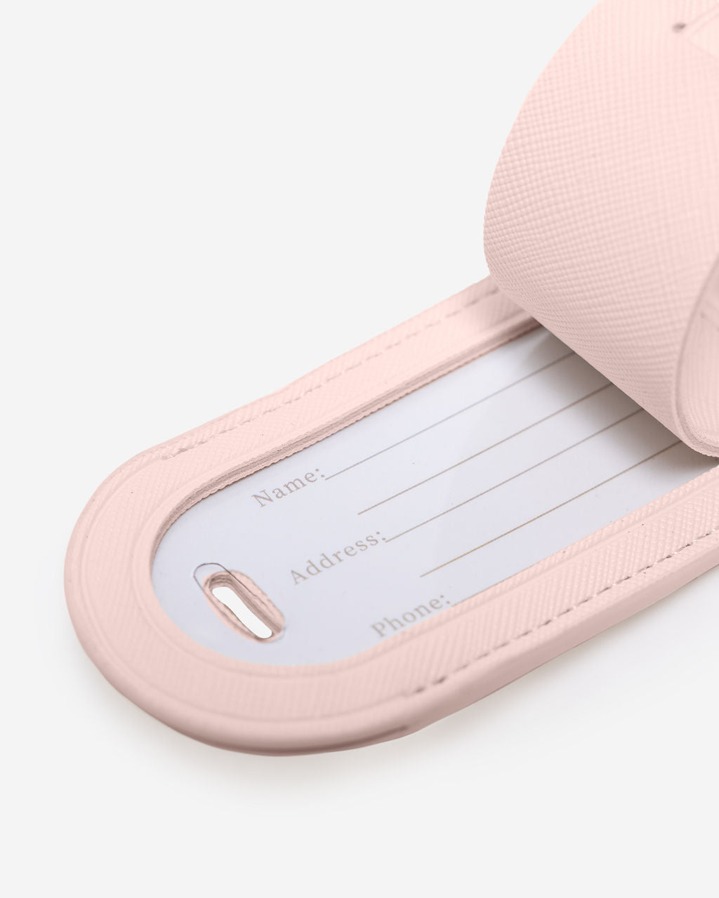 Close-up of a light pink Saffiano leather luggage tag with the internal white card showing fields for Name, Address, and Phone.