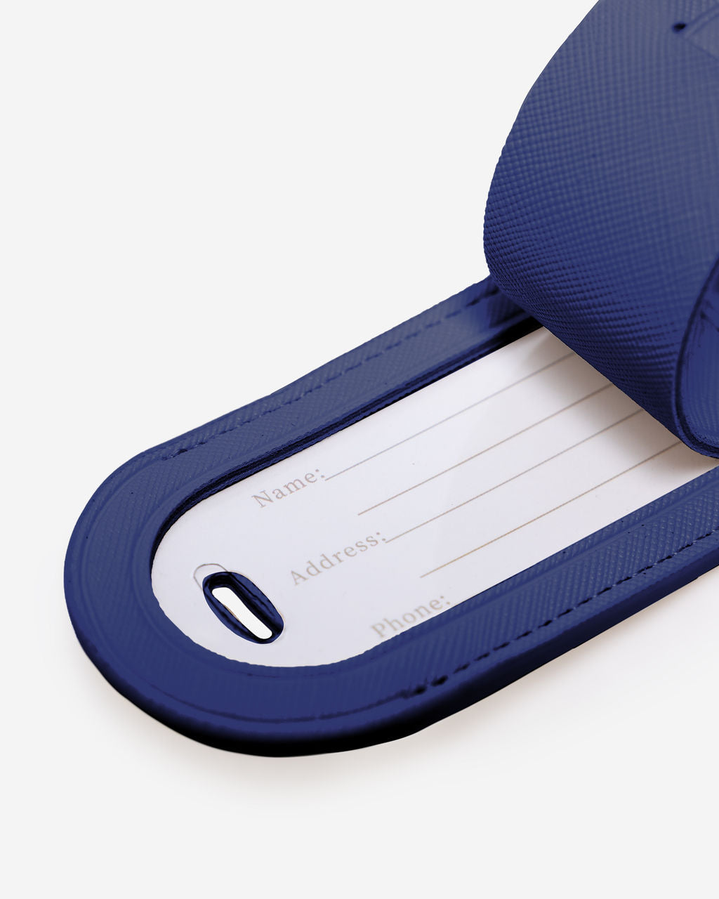 Close-up of a blue Saffiano leather luggage tag showing the internal white card with Name, Address, and Phone fields.