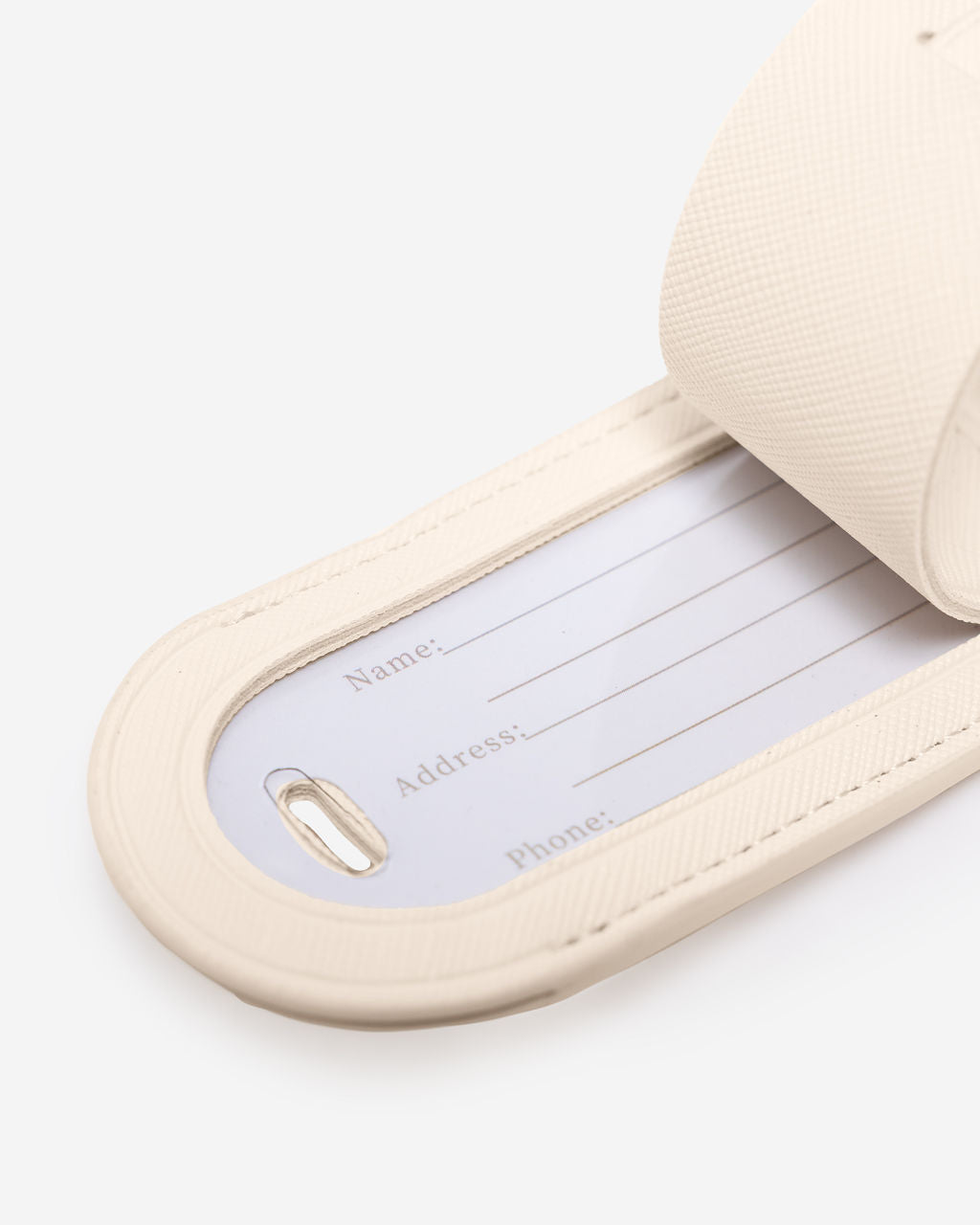 Close-up of a cream Saffiano leather luggage tag with the internal white card showing fields for Name, Address, and Phone.